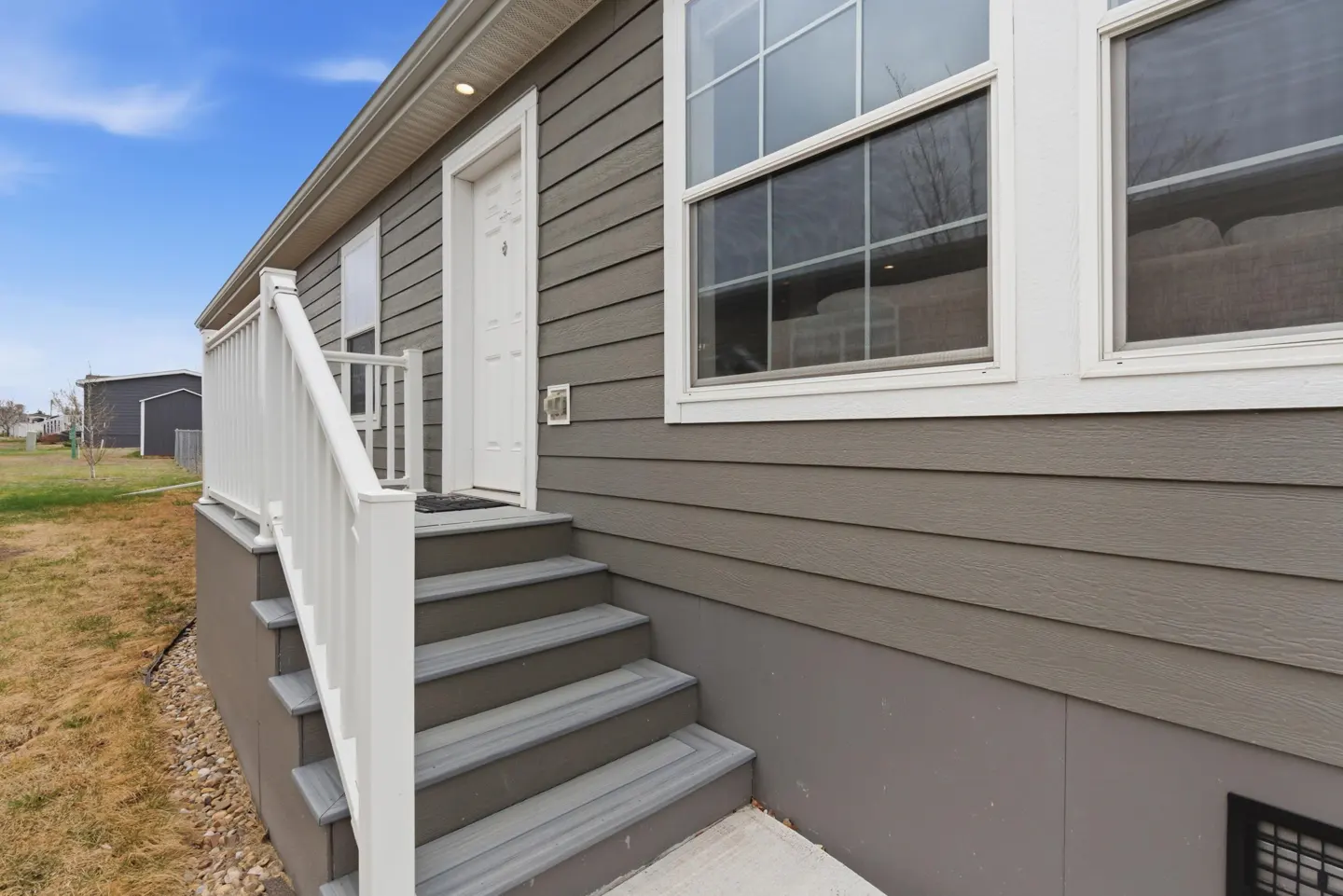 Exterior view of a gray house with white trim, a white front door, and gray steps with a white railing.