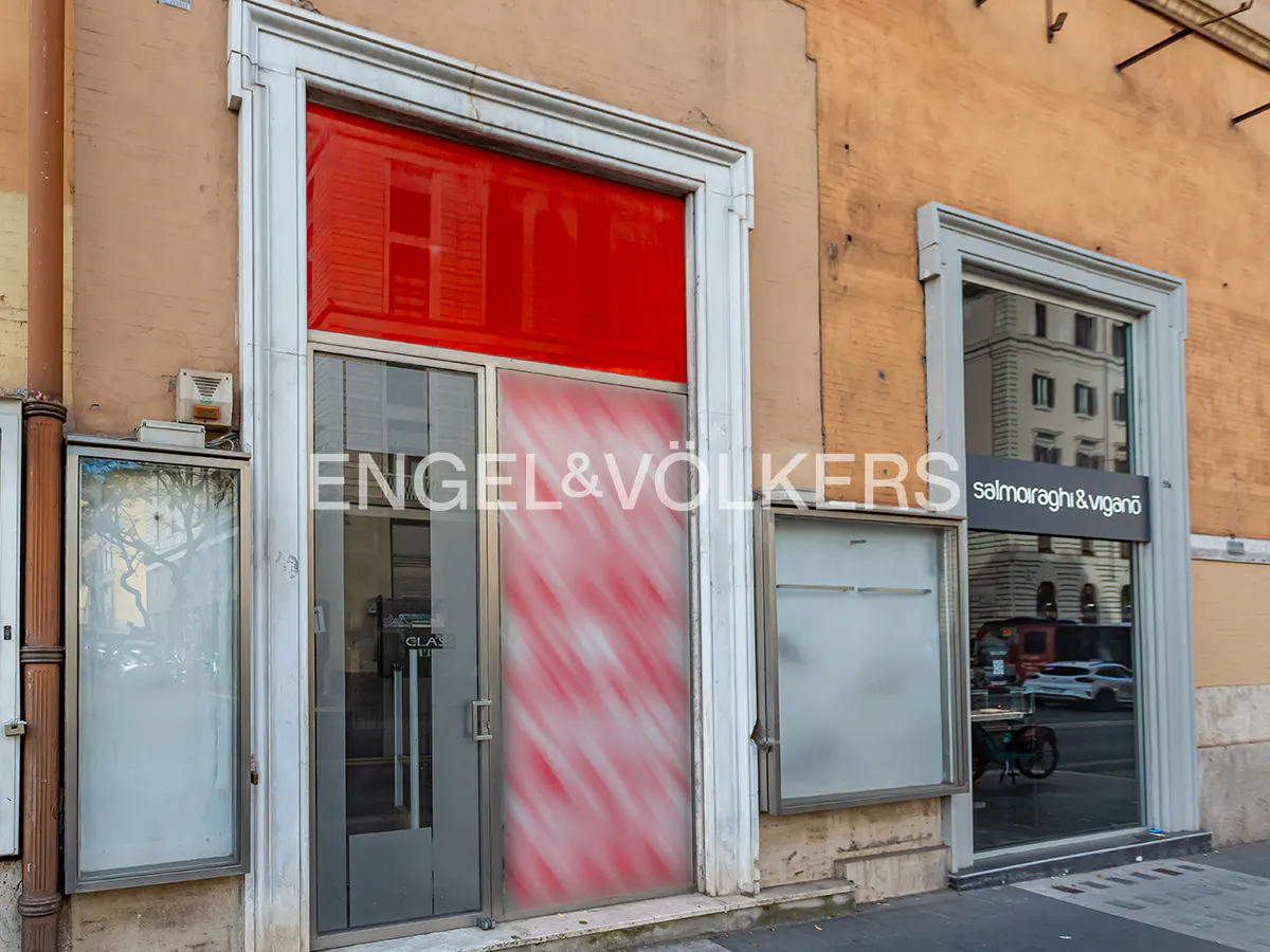Exterior view of Engel & Volkers real estate office with red and white window film, next to Salmoiraghi & Viganò store.