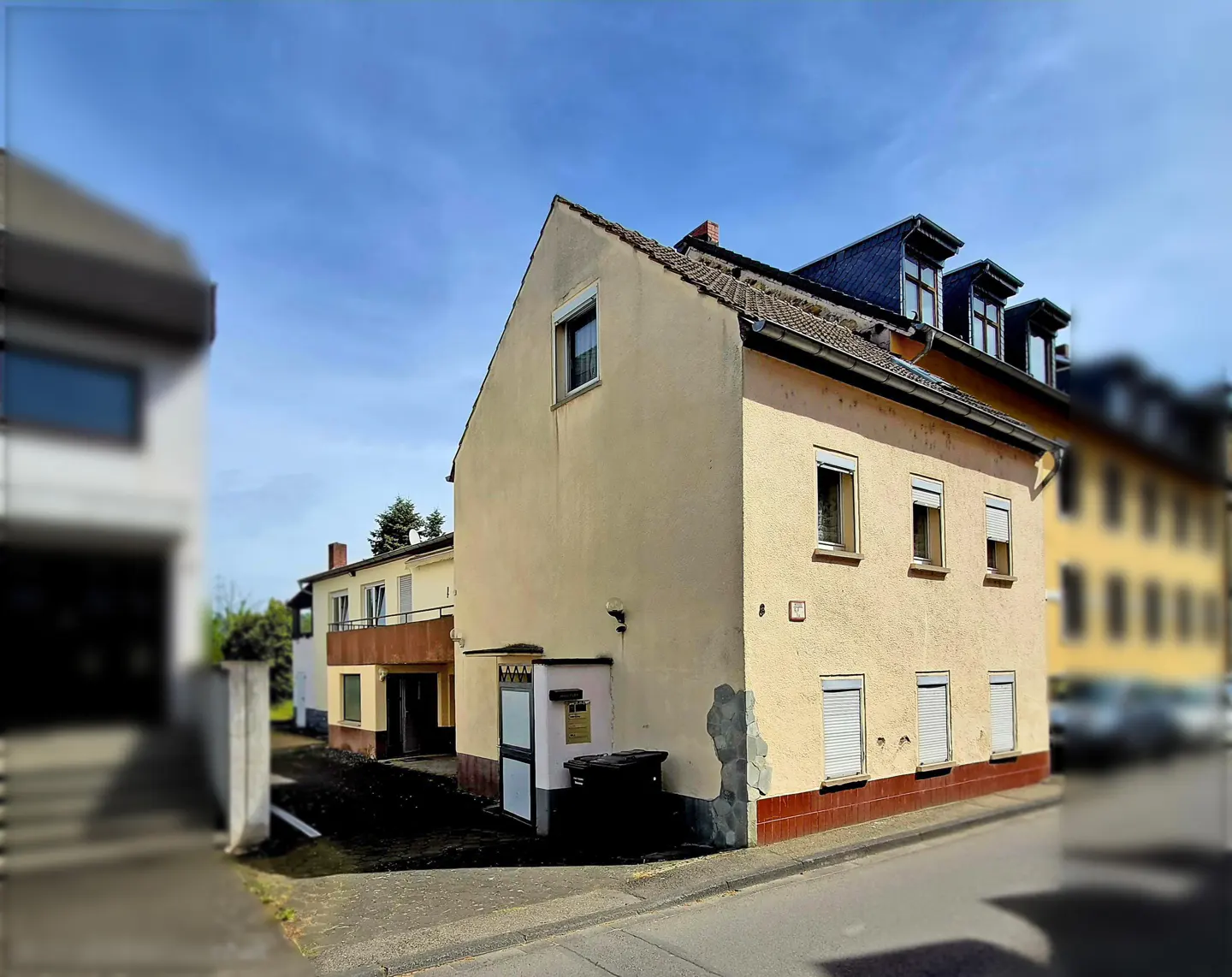 Two-story yellow house with a red brick foundation and a gray roof on a sunny day.