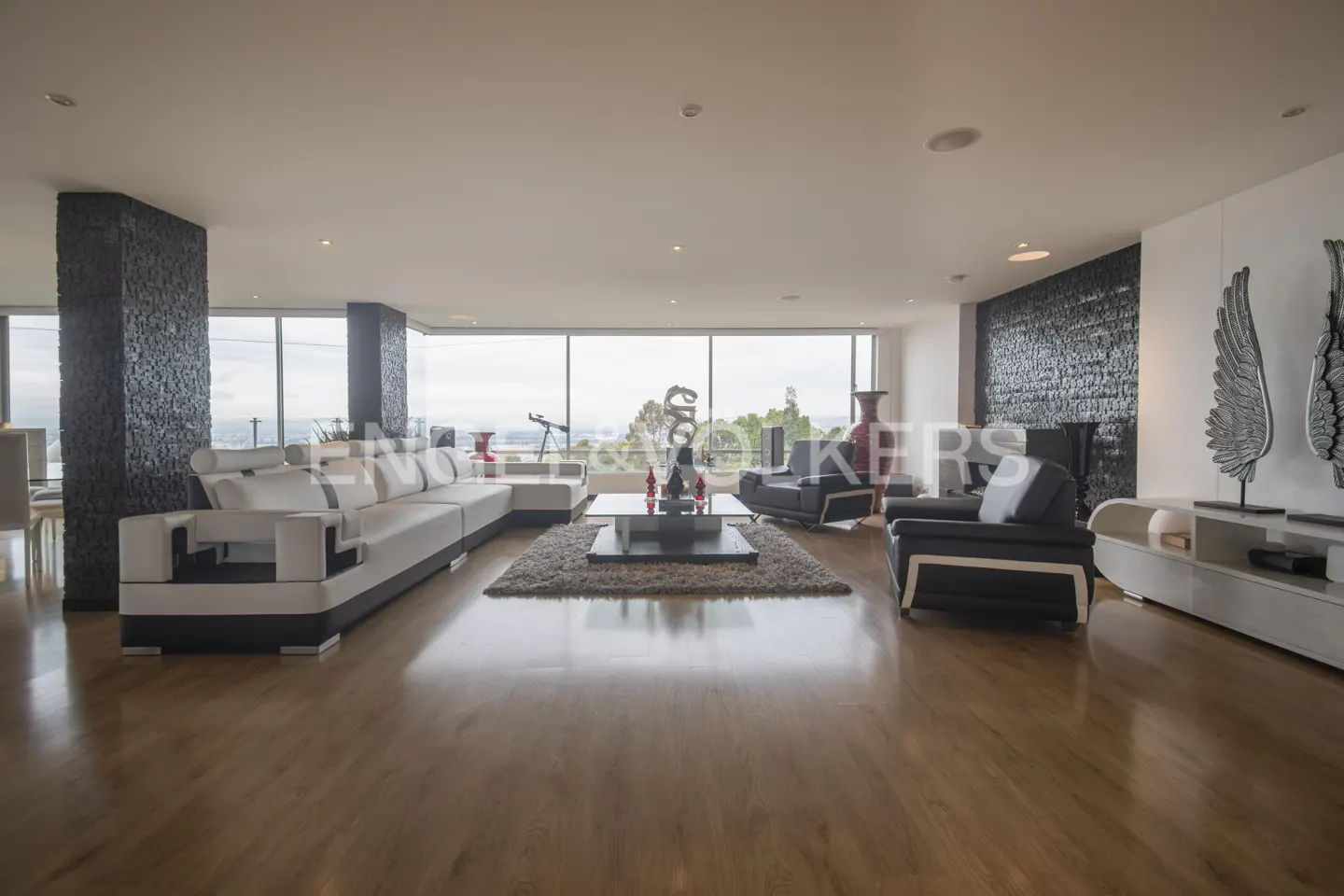 A spacious living room with a white sectional sofa, black armchairs, and a large window with a view.