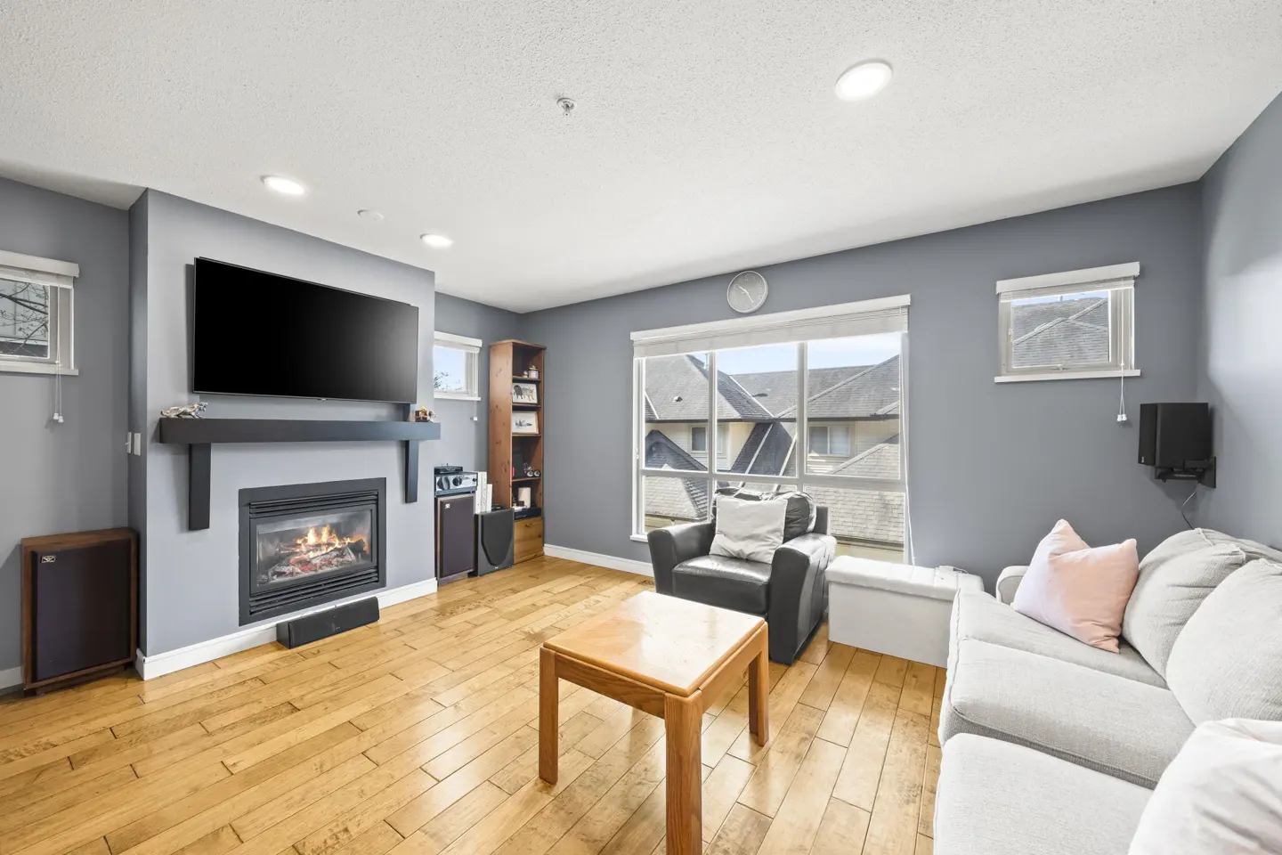 Living room with gray walls, wood floors, and a fireplace with a TV above it. There is a gray sofa, a black armchair, and a wood coffee table.