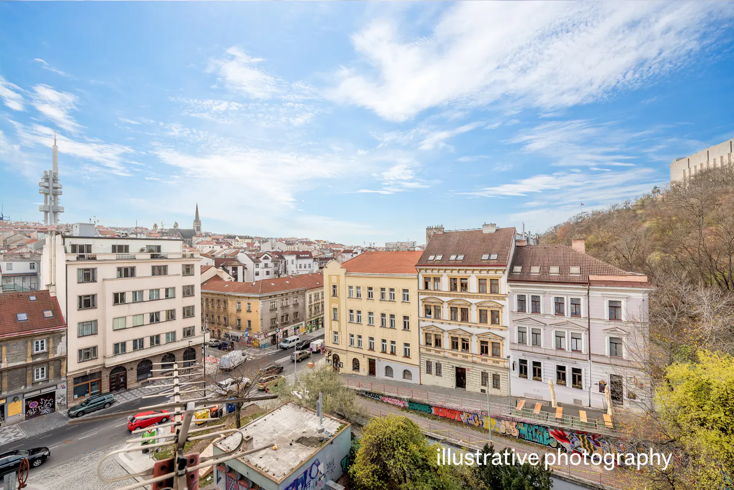 Cityscape view of Prague, Czech Republic, with colorful buildings, a TV tower, and a blue sky with clouds.