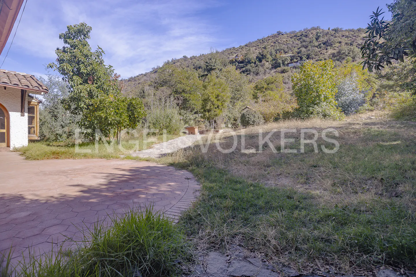 Exterior view of a house with a red stone patio, a grassy yard, and a mountain in the background on a sunny day.
