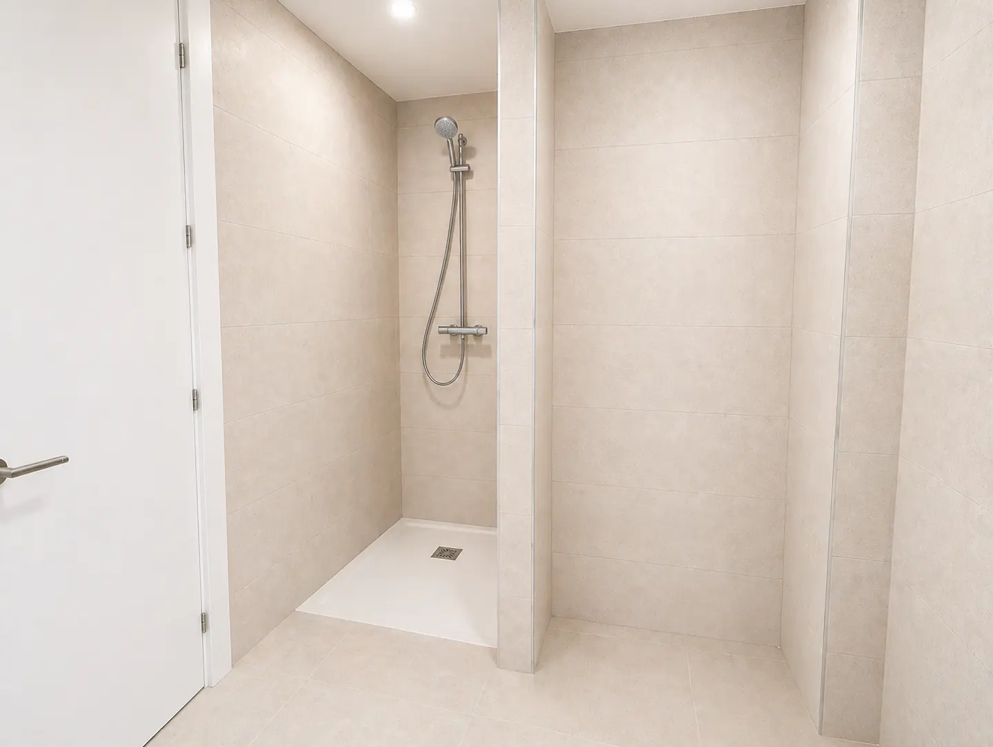 A modern bathroom with beige tile walls, a white door, and a walk-in shower with a silver shower head.