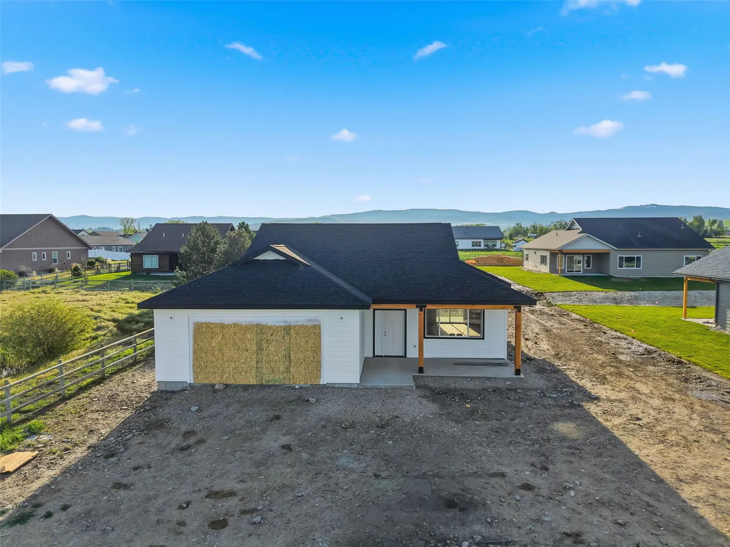 A white, single-story house with a black roof and boarded-up garage under a blue sky.