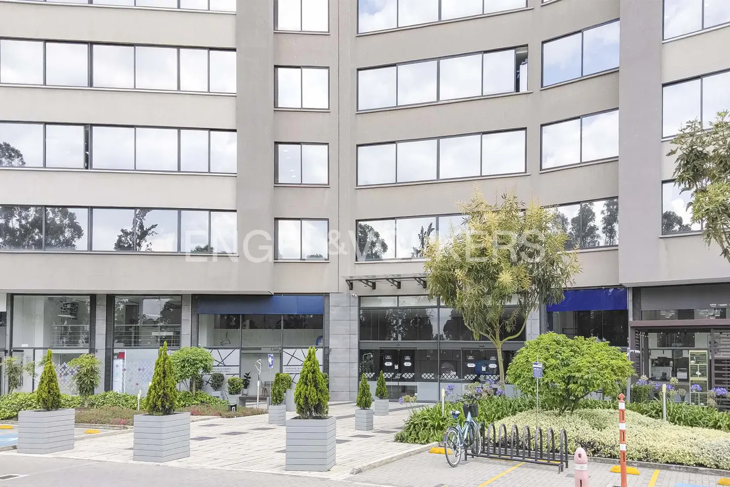 Exterior of a modern, multi-story building with large windows, landscaping, and a bike rack.