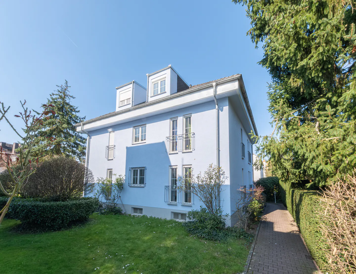 Light blue two-story building with small balconies, green lawn, and brick walkway under a clear blue sky.