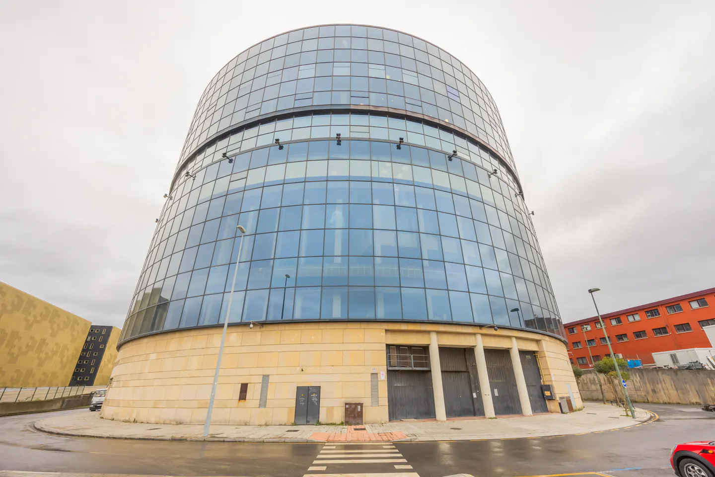 Exterior view of a modern, curved glass building with a stone base on a cloudy day.