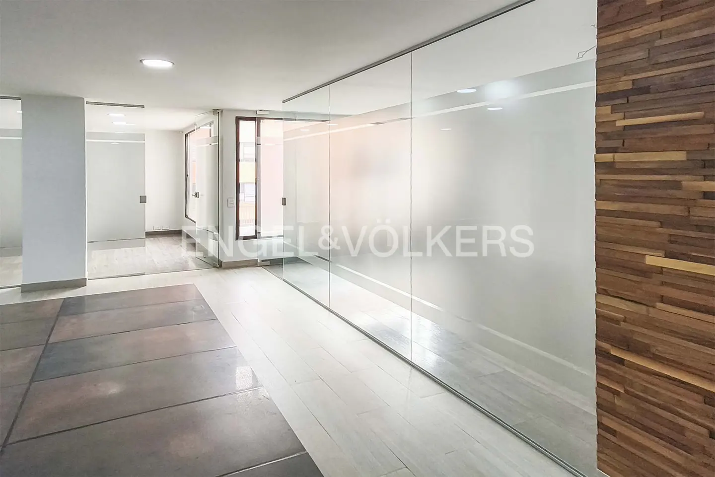 Bright office space with glass walls, wood accent wall, and concrete floors. Engel & Völkers logo on the glass.