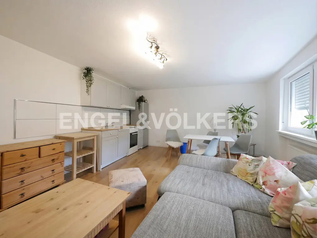 Open-plan living area with a grey sofa, wooden coffee table, dining set, and a modern kitchen with light grey cabinets.
