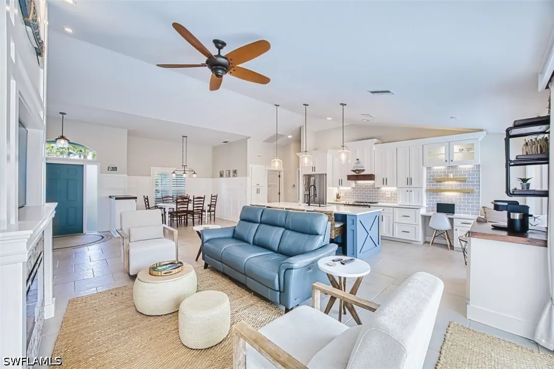 Open-concept living space with blue leather sofa, white chairs, kitchen island, and dining table.