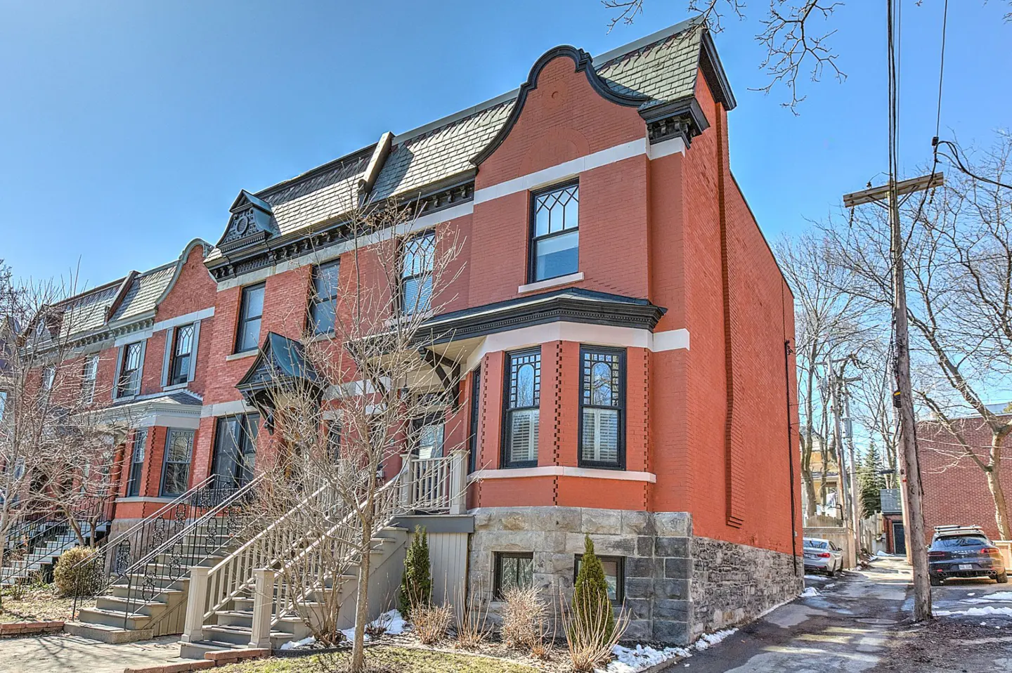 Exterior view of red brick row houses with grey roofs and stone foundations on a sunny day.