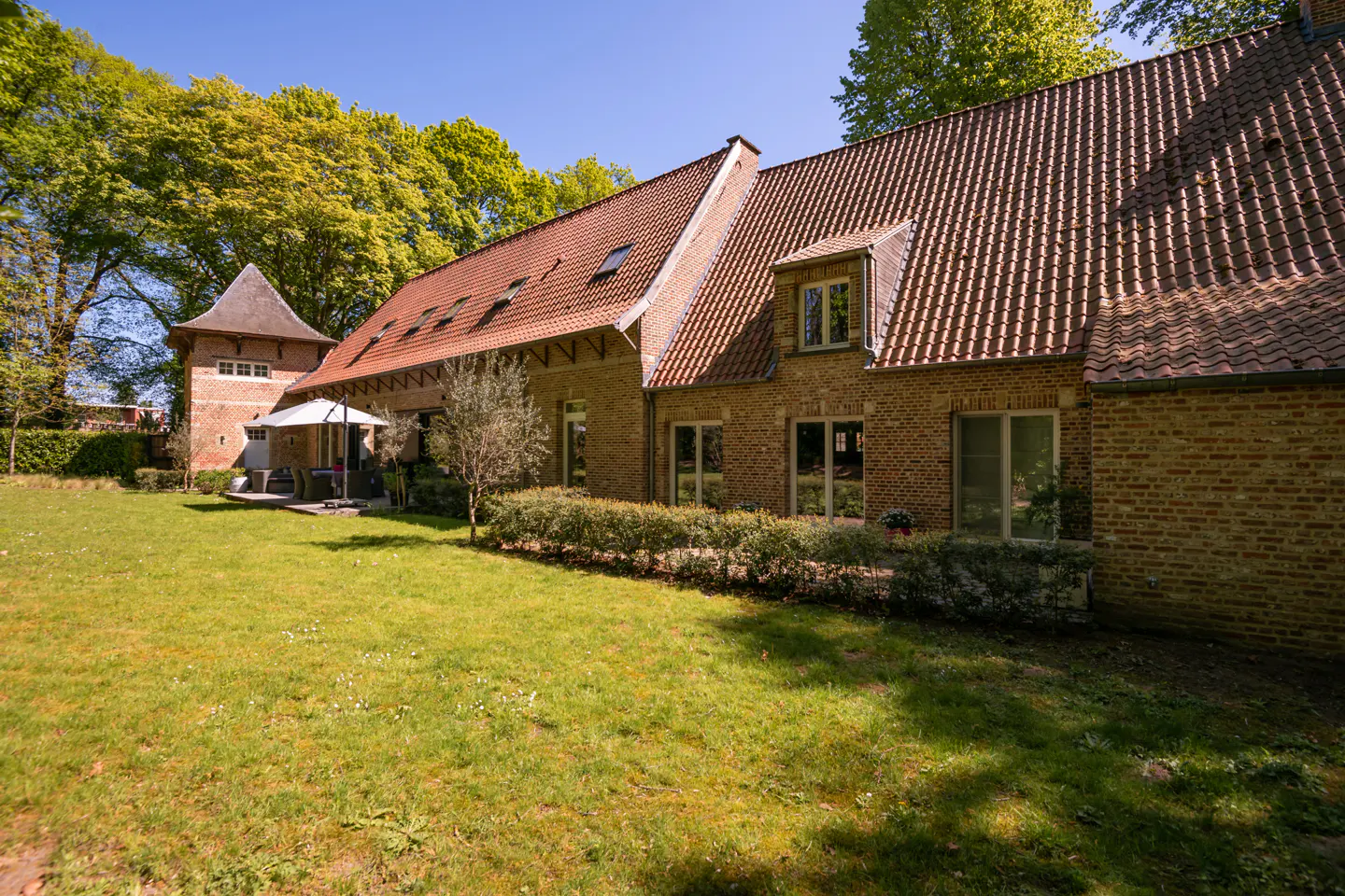Exterior view of a brick house with a red tile roof and green lawn. A turret is visible on the left.
