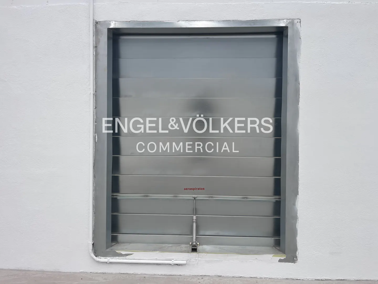 A large, metallic industrial louvered vent set into a plain white exterior wall, with Engel & Völkers branding overlaid.