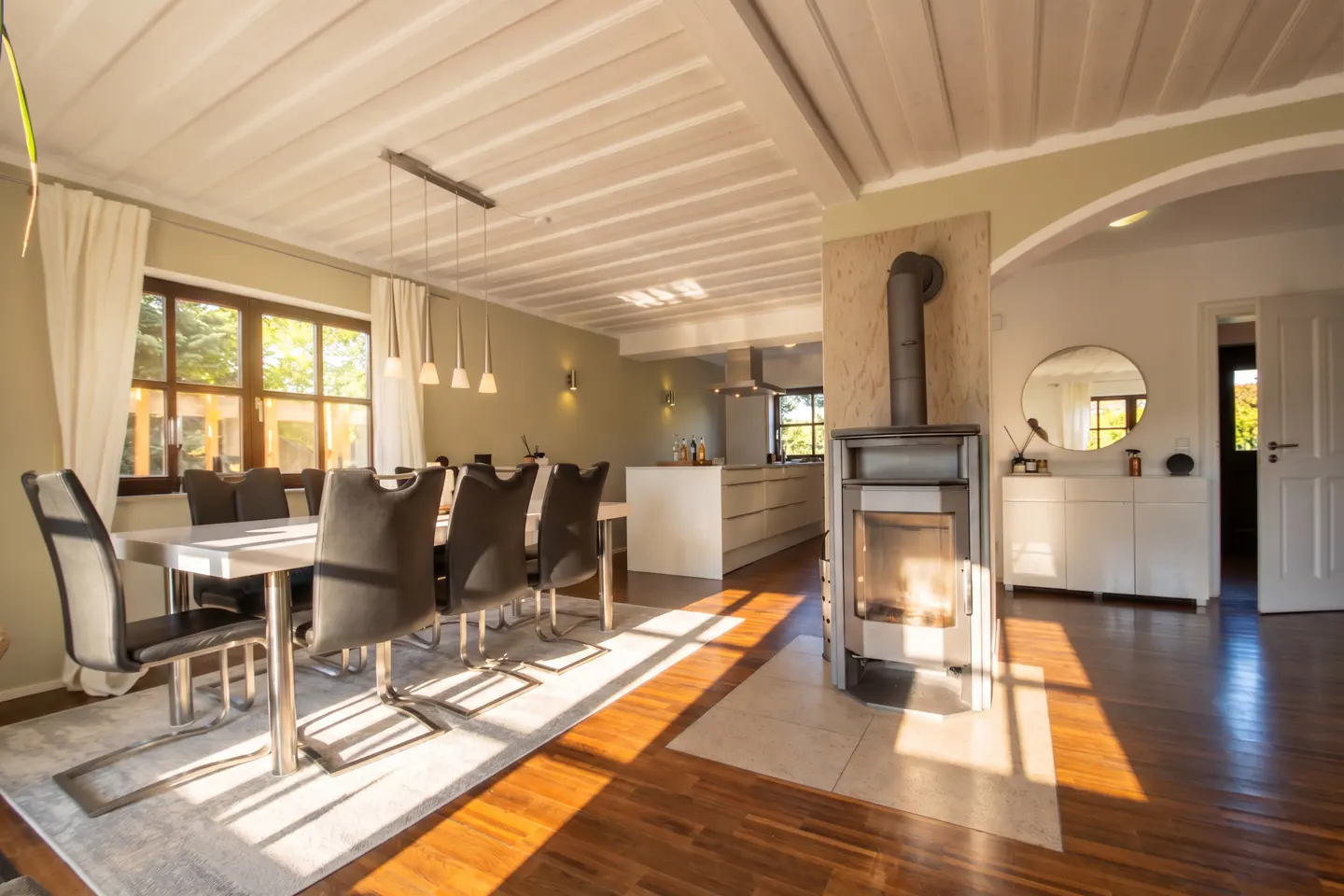 Bright, open-concept home interior with wood floors, dining table, fireplace, and kitchen in the background.