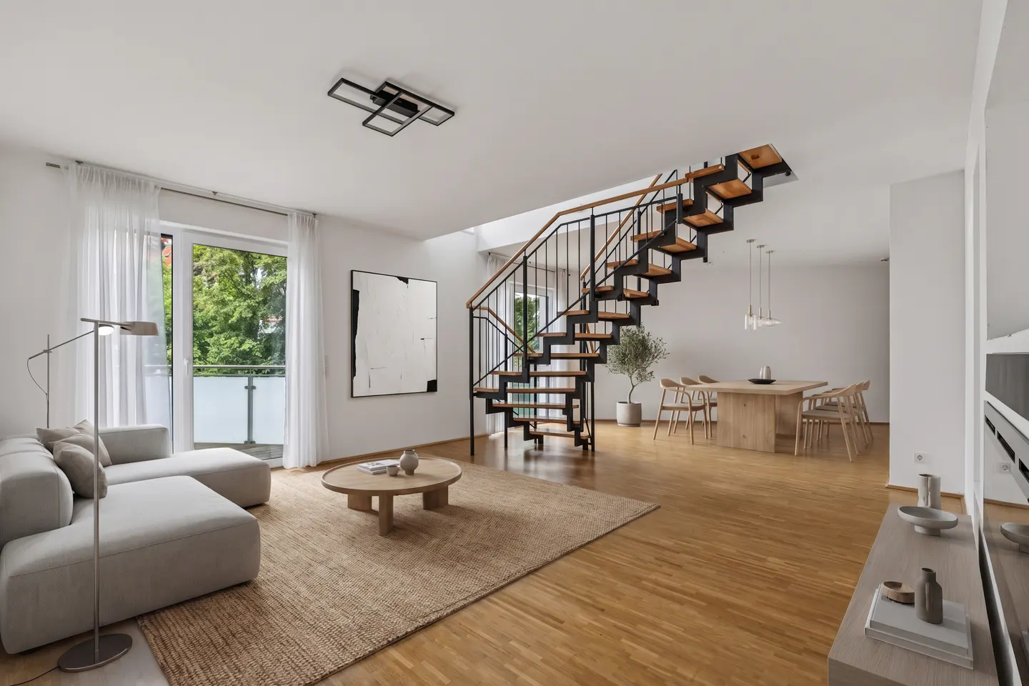 Modern open-plan living room with a light gray sofa, wooden coffee table, dining area, and a floating black metal staircase.