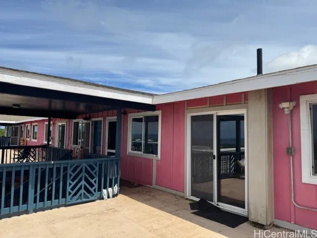 Exterior view of a pink building with white trim, sliding glass doors, and a blue railing under a cloudy sky.