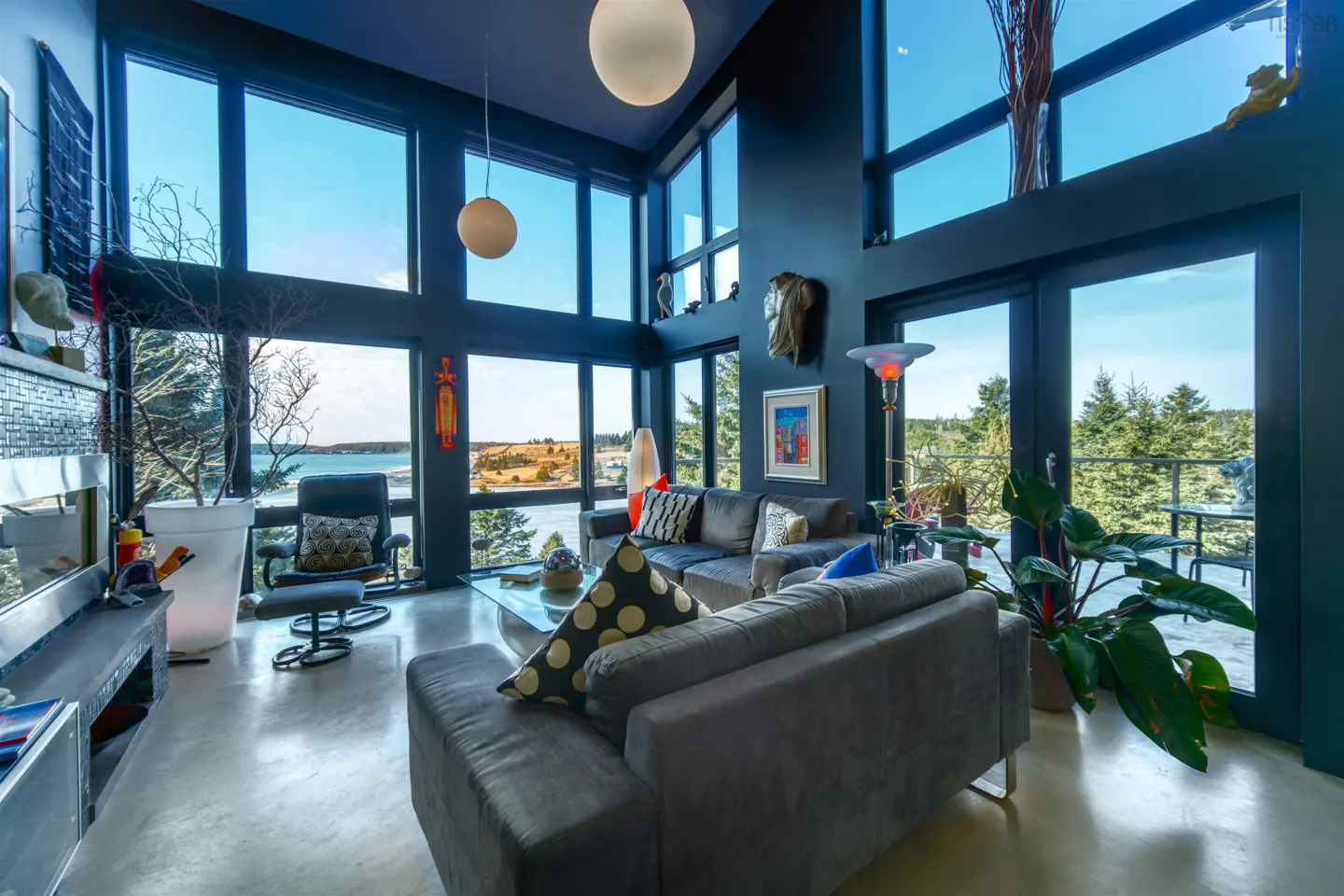 Modern living room with dark walls, floor-to-ceiling windows, gray sofas, and a scenic ocean view.