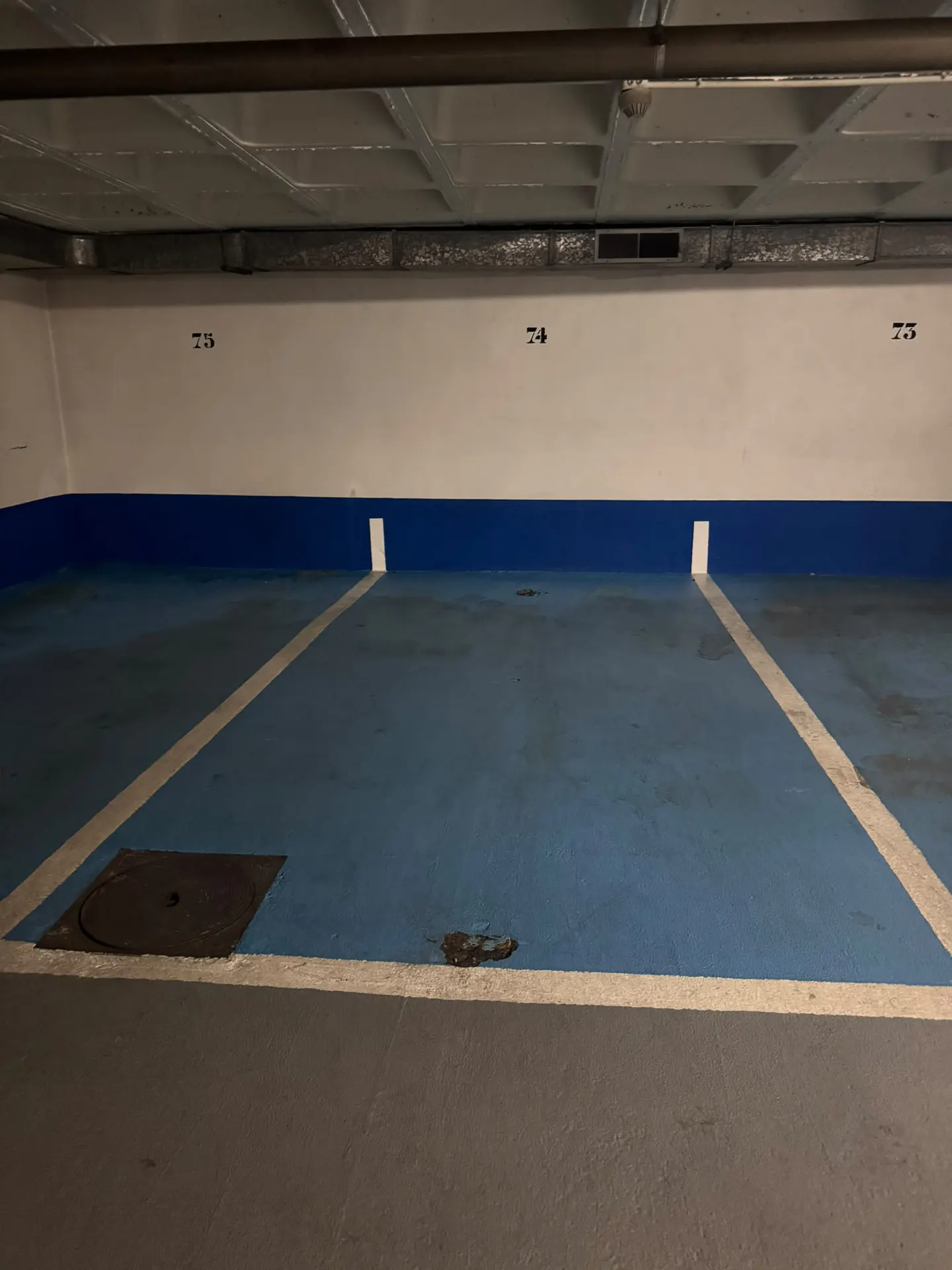 Empty indoor parking spaces numbered 73, 74, and 75 with blue painted floors and white parking lines in a concrete garage.