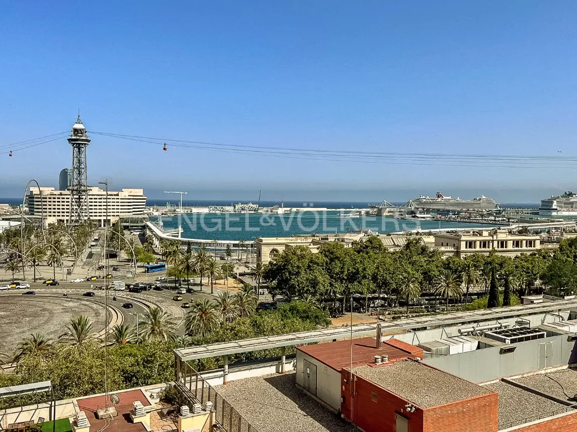 Barcelona cityscape view from a rooftop, featuring the port, cable cars, and palm trees under a clear blue sky.
