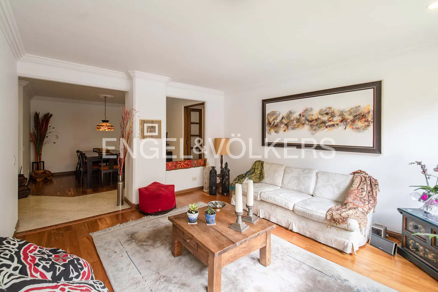 Living room with white sofa, wooden coffee table, and hardwood floors. Dining room visible in background. Artwork on wall.