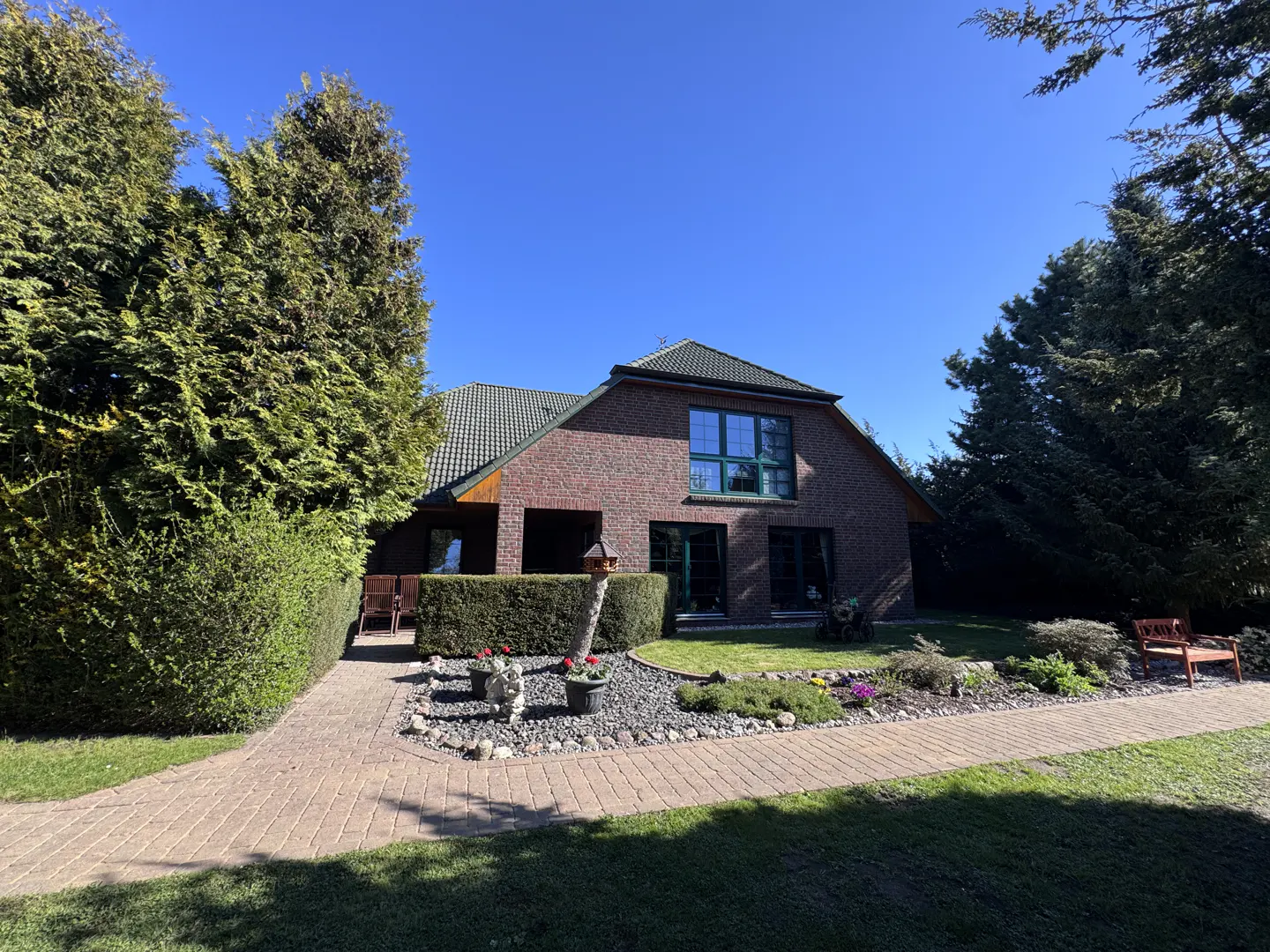 Brick house with green trim and roof, surrounded by trees and a garden. A stone path leads to the entrance.