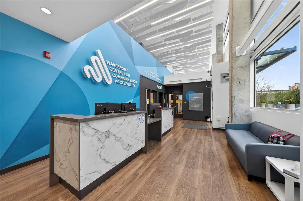 Office reception area with a marble counter, blue accent wall with the company logo, and a blue sofa near a window.
