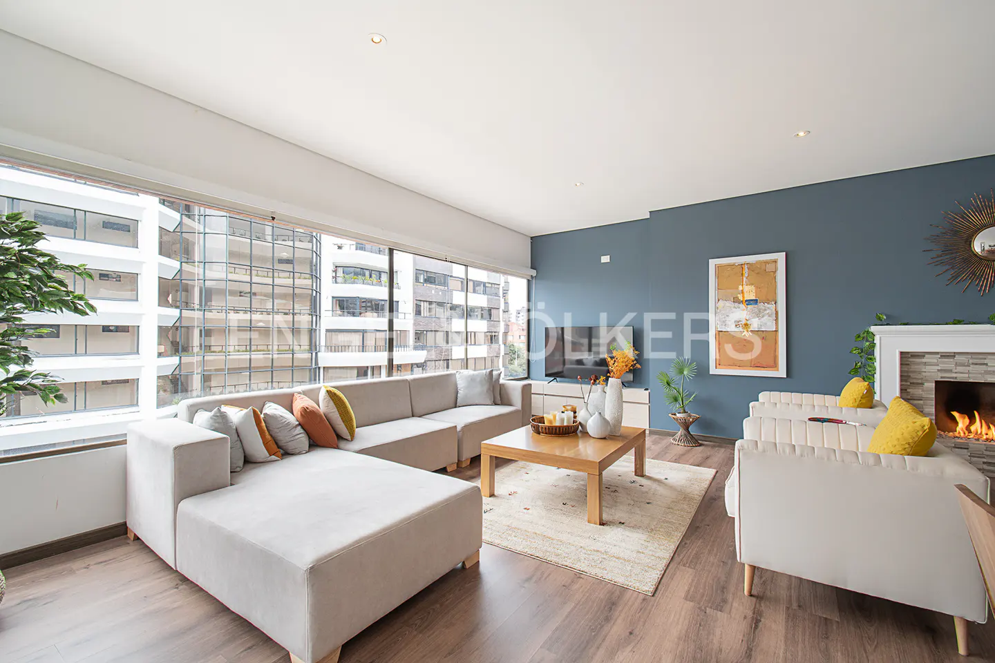 Bright living room with a large window, beige sectional sofa, wood floors, and a fireplace.