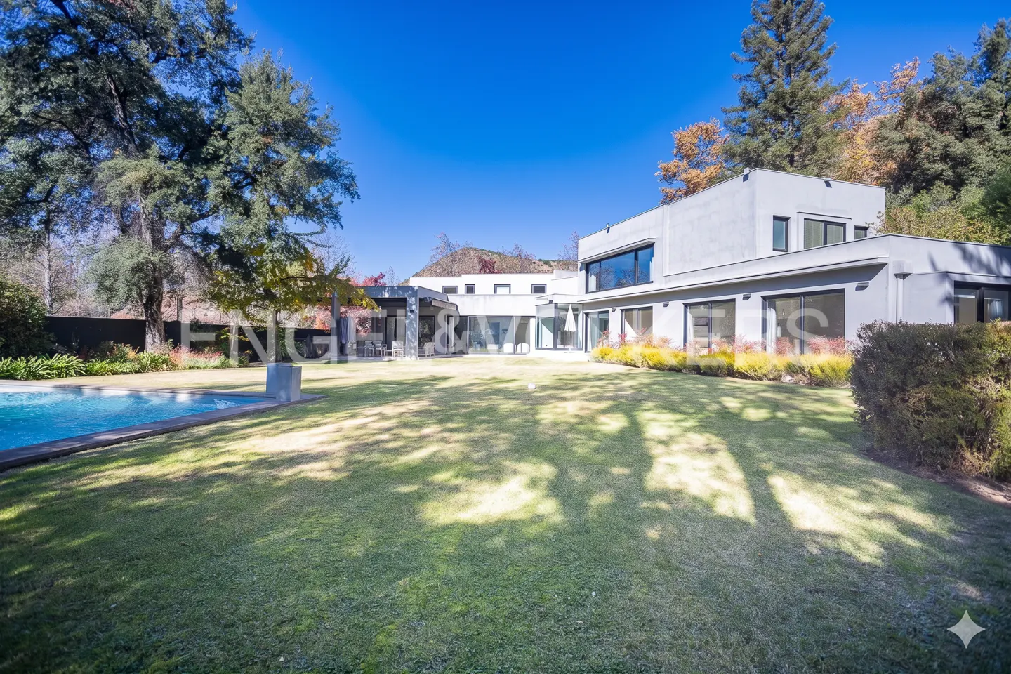 Exterior of a modern gray house with a pool and large lawn under a clear blue sky.