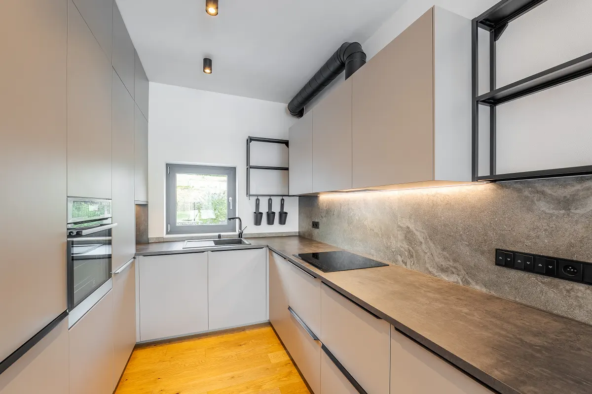 Modern kitchen with light gray cabinets, wood floors, and gray countertops. A black sink and oven are visible.