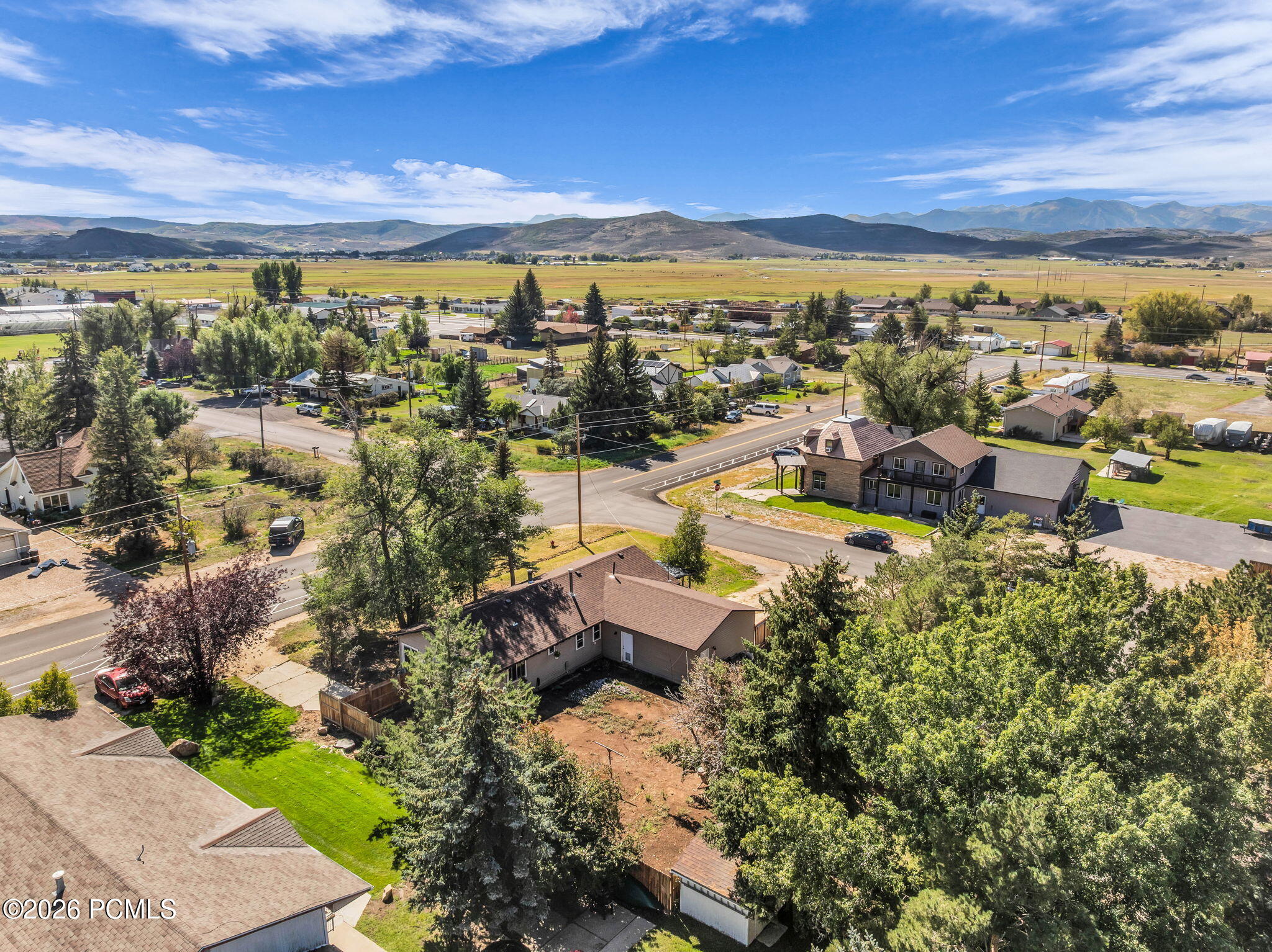 Aerial view of a residential neighborhood with houses, green trees, and roads under a blue sky with distant mountains. [AI-generated text]