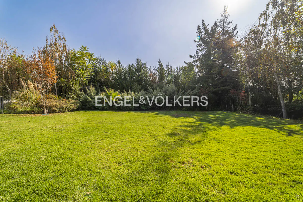 Lush green lawn with trees and shrubs in the background. The Engel & Völkers logo is superimposed on the image.