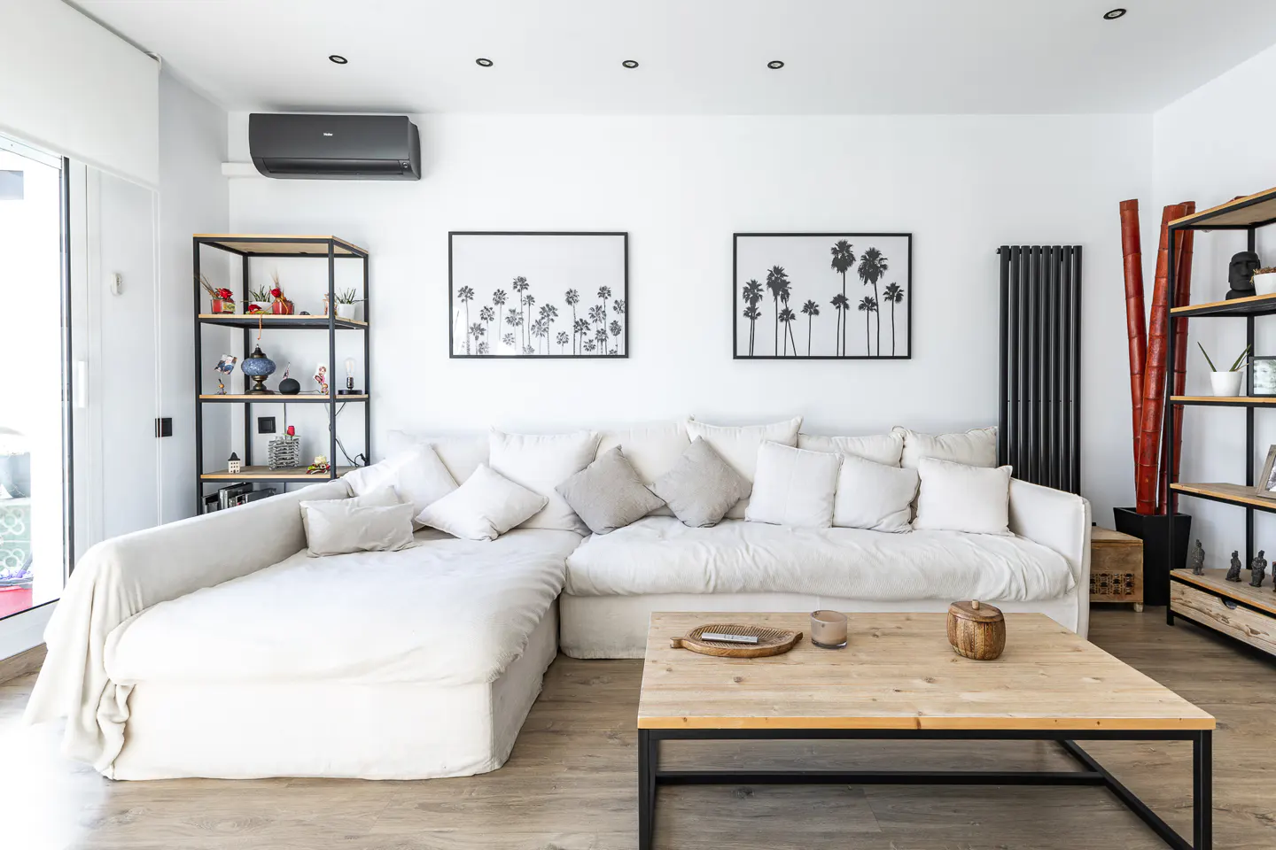 Bright living room with a white sectional sofa, wood coffee table, and palm tree art prints on a white wall.