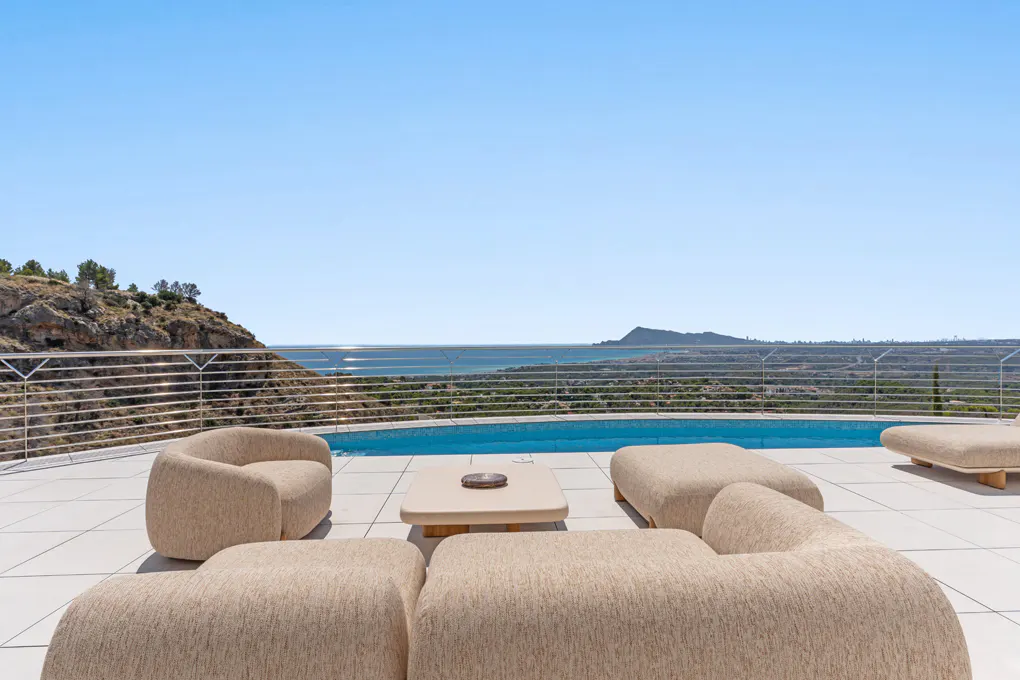 Outdoor patio with beige seating, a pool, and ocean views under a clear blue sky.