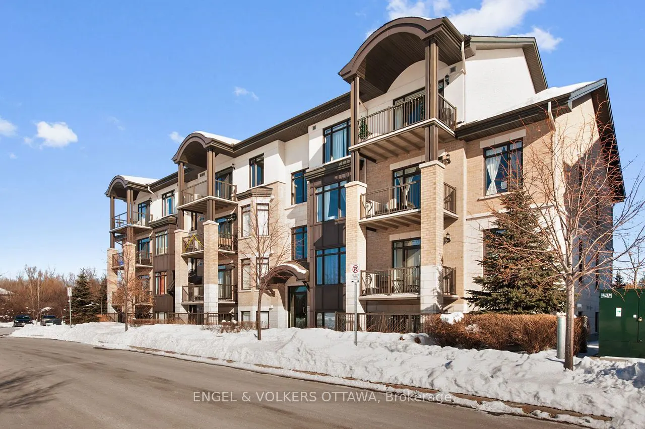 Three-story brick apartment building with balconies on a sunny winter day. Snow lines the street and landscaping.
