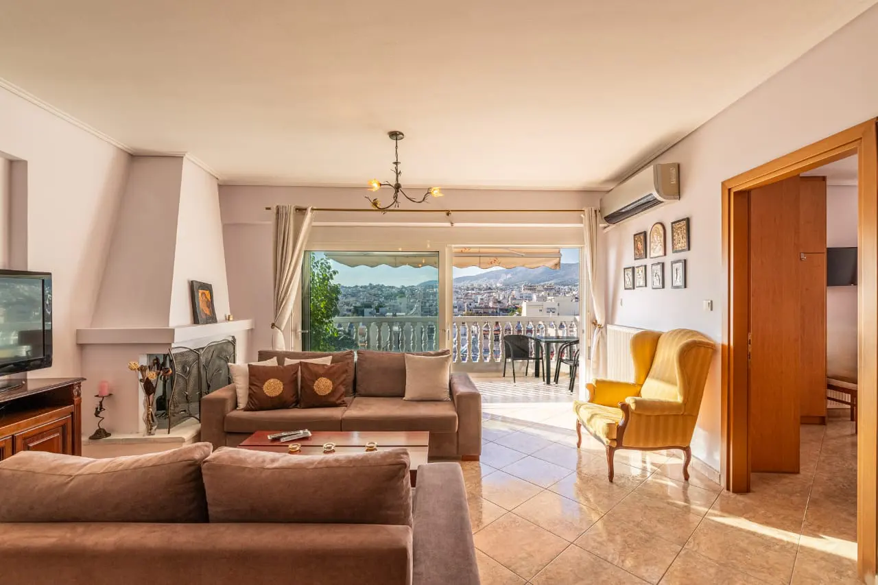 Living room with brown sofas, yellow armchair, fireplace, and balcony with city view.