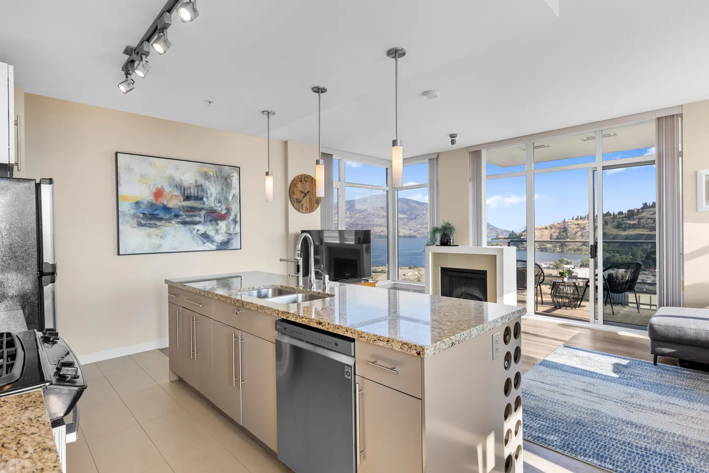 Modern kitchen island with granite countertop, stainless steel appliances, and a scenic lake view through floor-to-ceiling.