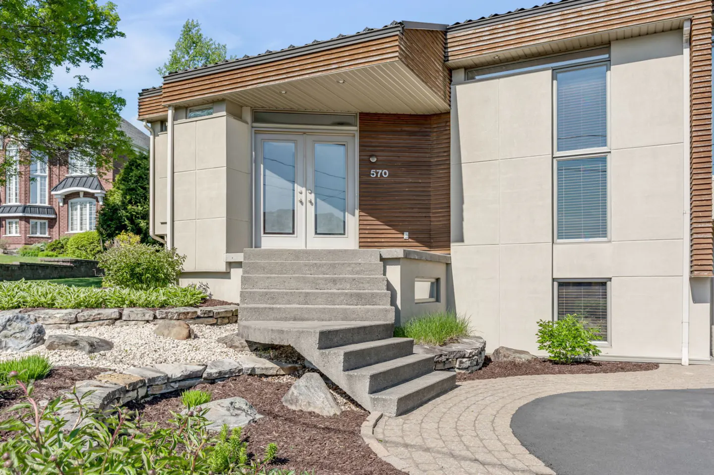 Modern home exterior with wood siding, concrete stairs leading to double front doors, and a landscaped front yard.