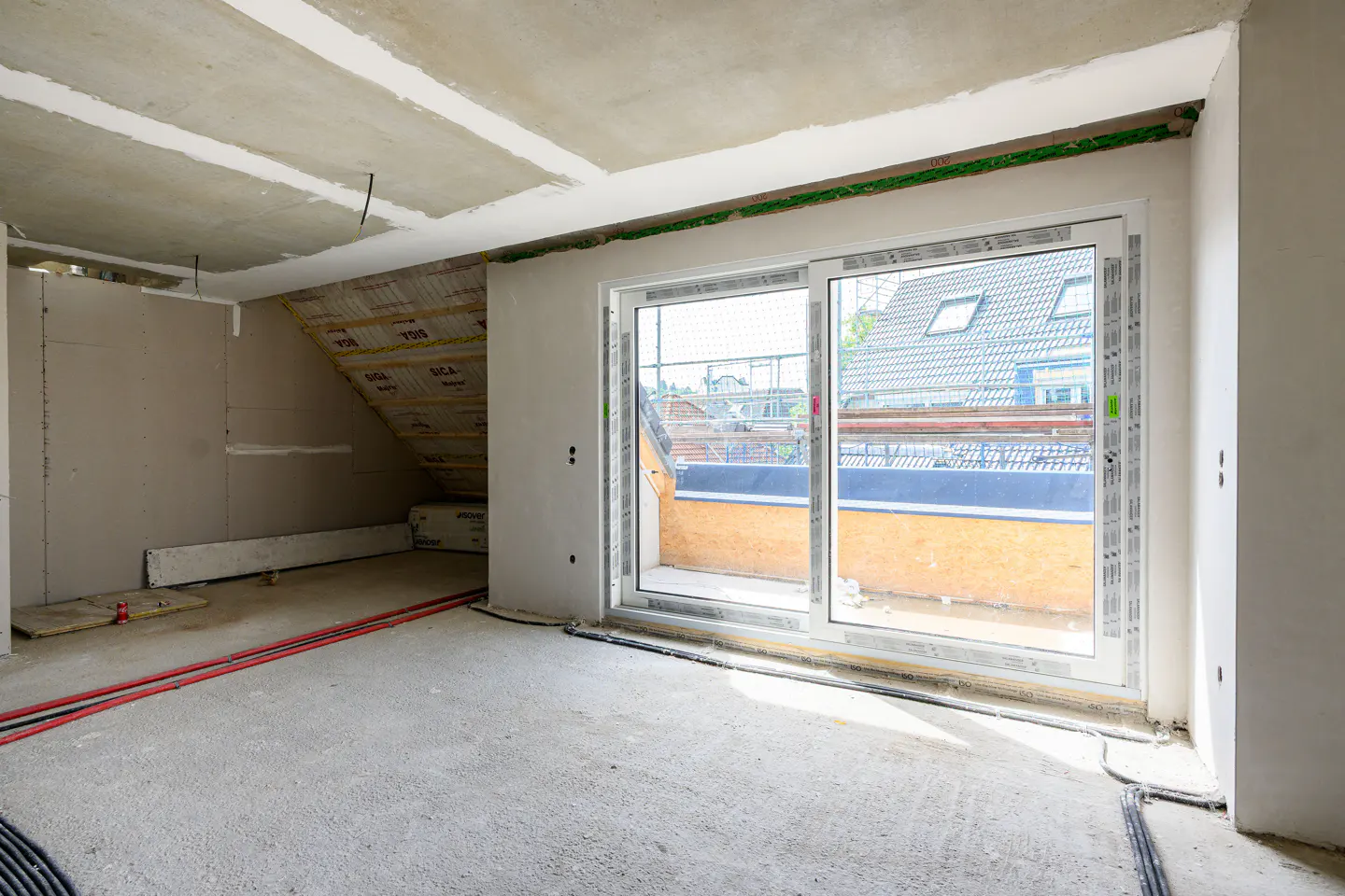 Unfinished room with concrete floor, exposed ceiling, and large sliding glass doors to a balcony. Red and black cables run along the floor.