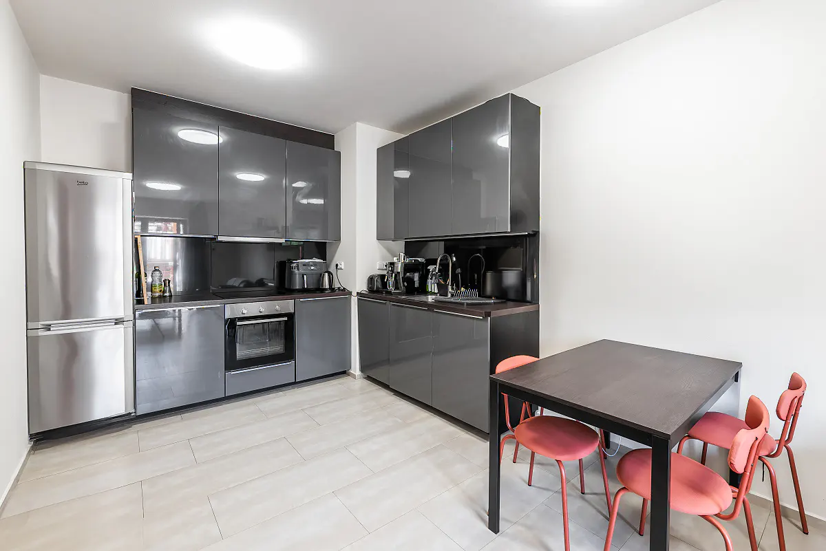 A modern kitchen with gray cabinets, stainless steel appliances, and a dark wood table with four red chairs.