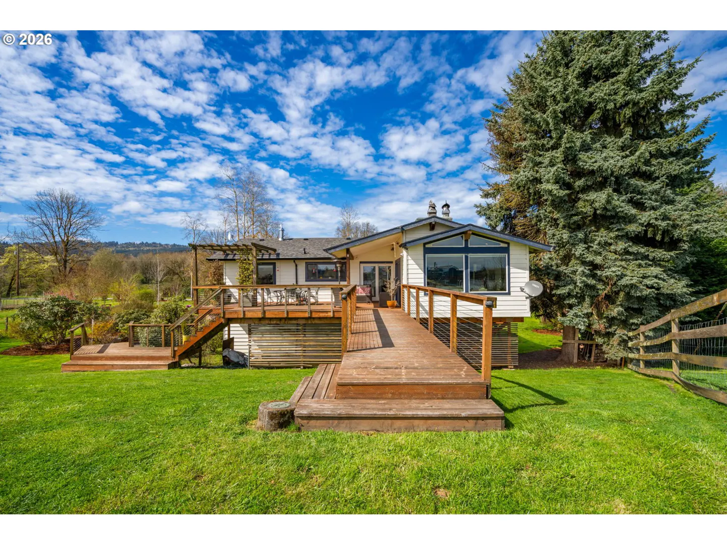 Exterior view of a white house with a wooden deck and ramp, green lawn, and blue sky.