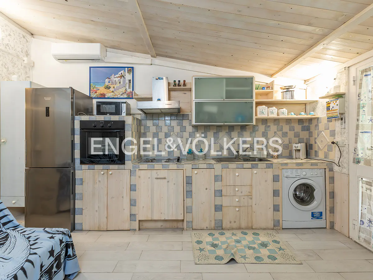 A bright kitchen with light wood cabinets, blue tile backsplash, stainless steel fridge, and a washing machine.