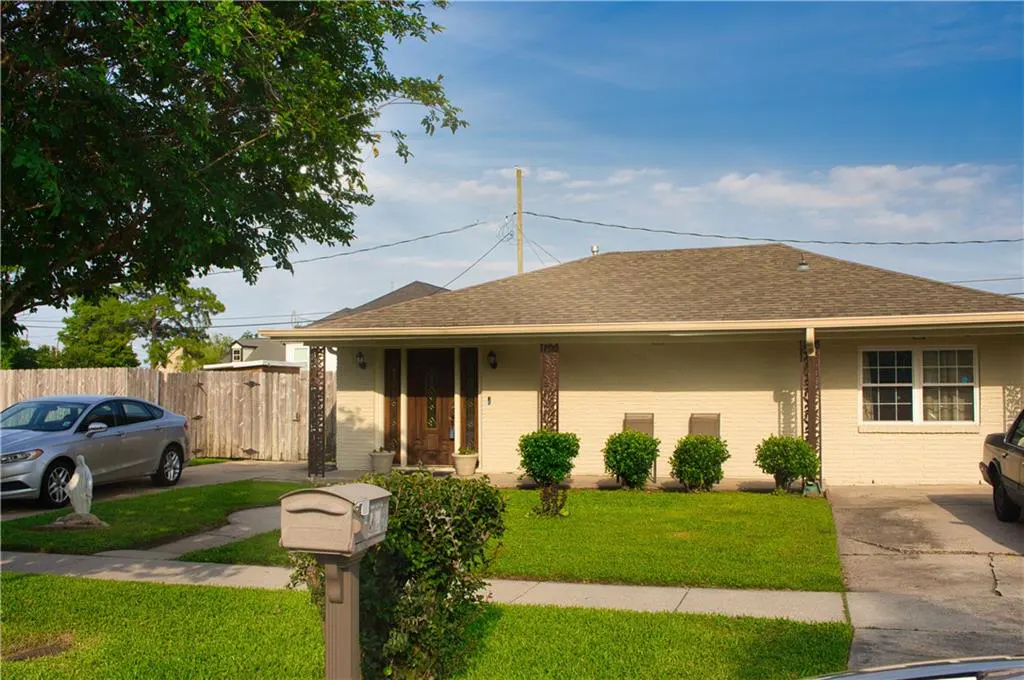 Beige single-story house with a brown roof, green lawn, and a silver car parked in the driveway.