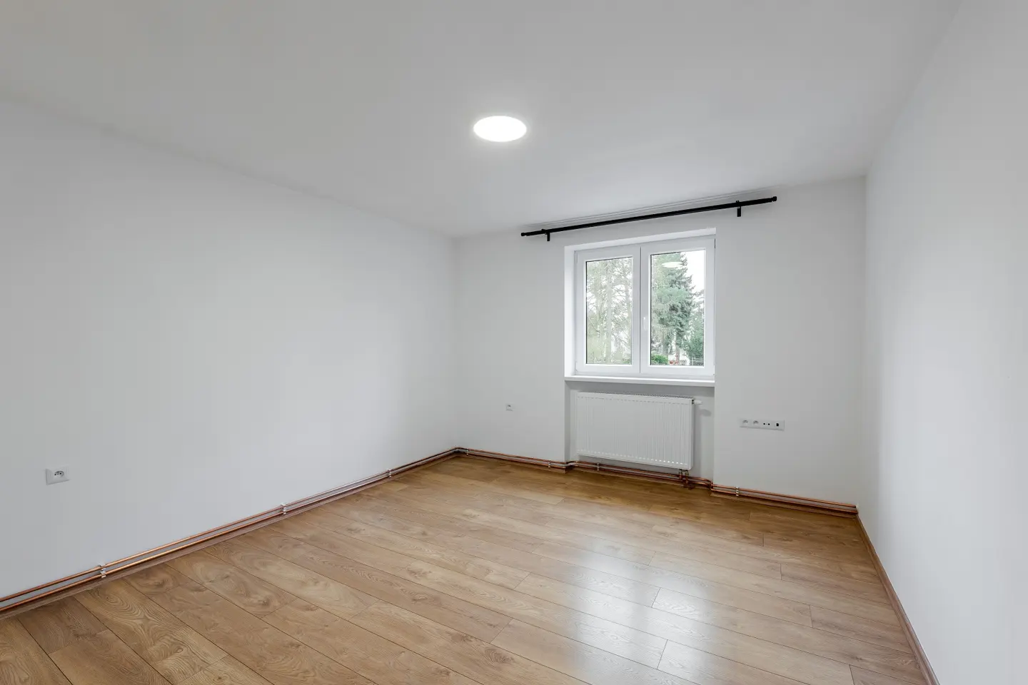 Empty room with white walls, wood floor, and a window. A radiator is under the window.