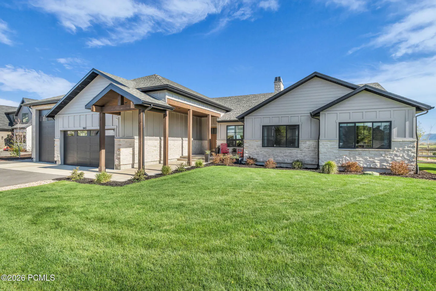 A modern, single-story home with gray siding, stone accents, and a dark gray roof under a bright blue sky. A green lawn extends to the front.