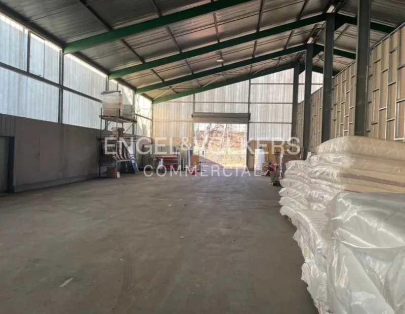 A large, empty warehouse with a metal roof and concrete floor. Stacks of wrapped materials are on the right.