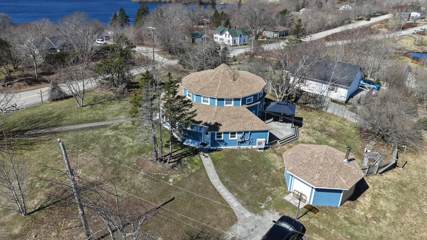 Aerial view of a two-story blue house with a brown roof, surrounded by trees and a green lawn. A stone path leads to the house.