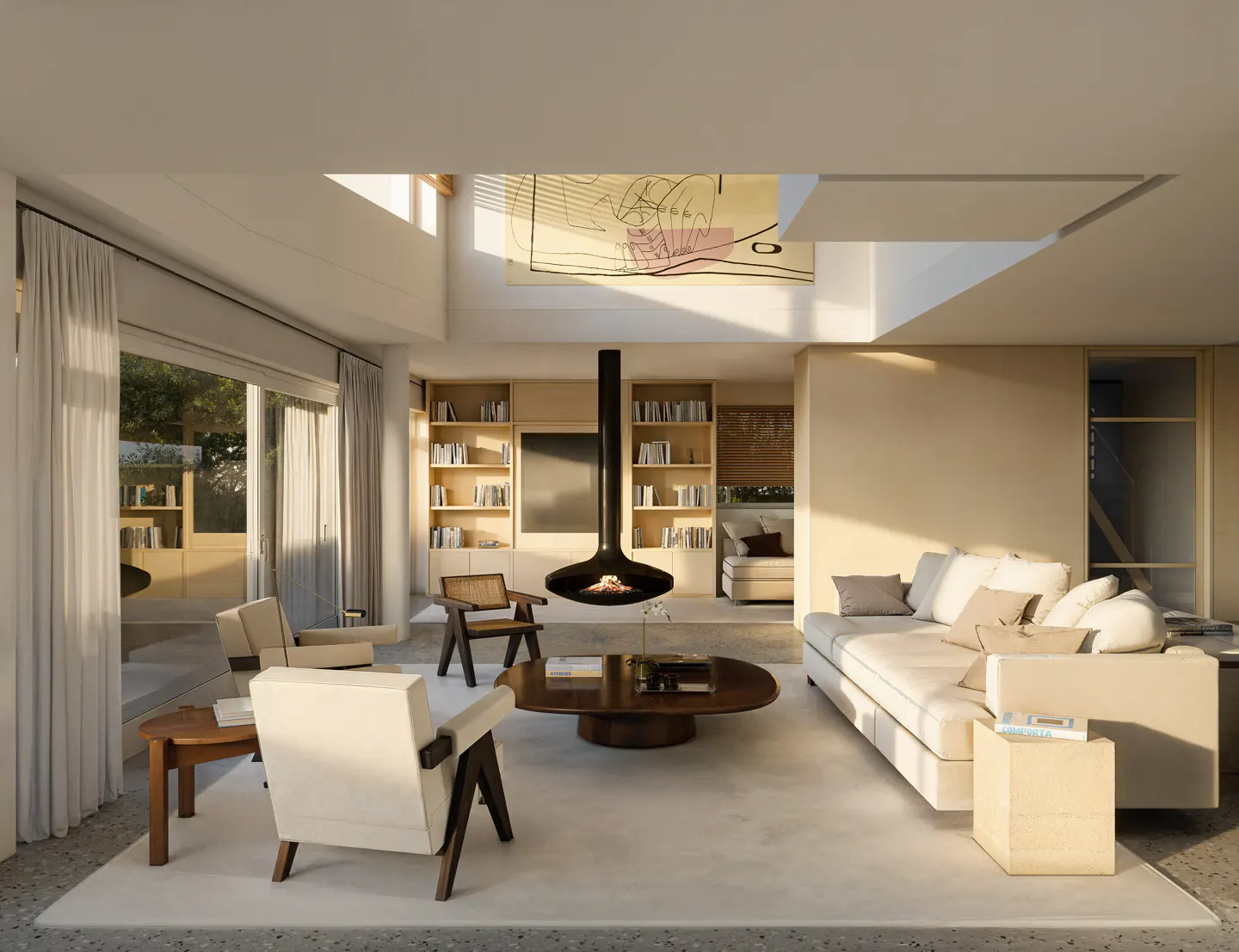 Bright living room with a black, hanging fireplace, light beige sofa, wooden chairs, and a large window with sheer curtains.