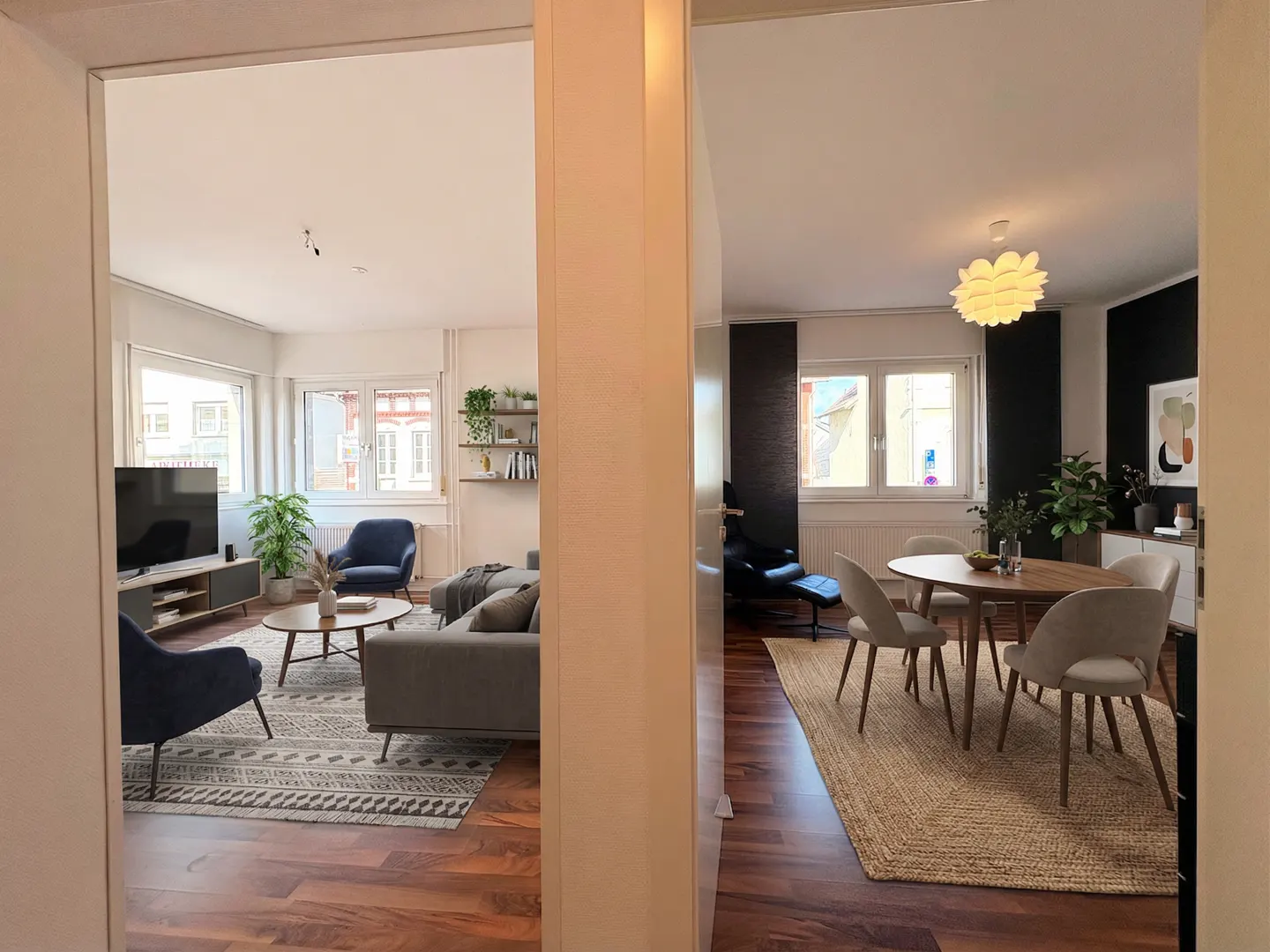 A view through a doorway shows a living room with a gray sofa and a dining room with a round table and chairs.