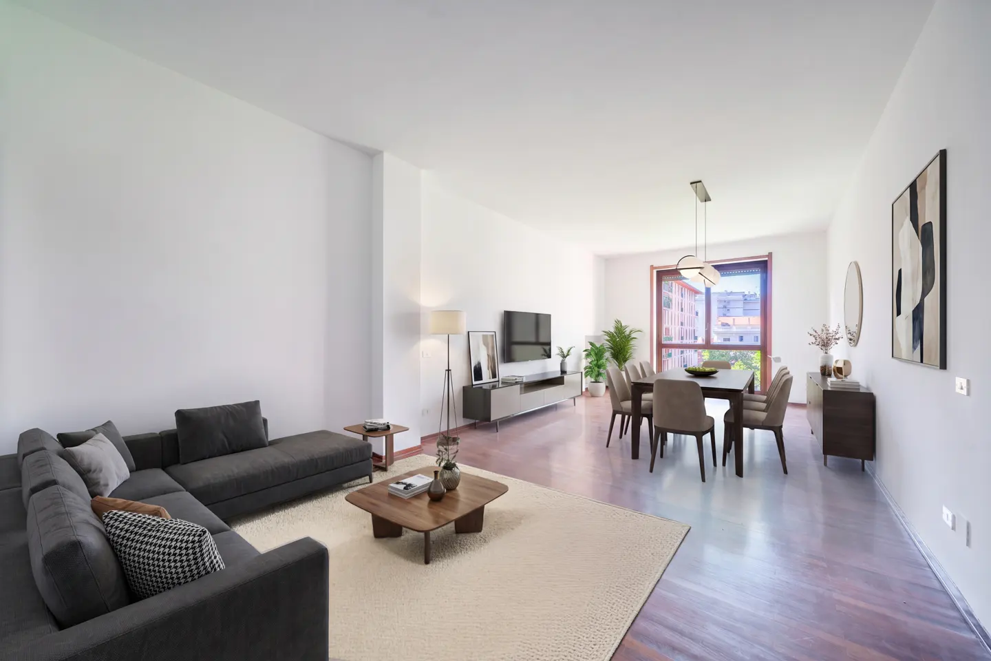 A modern living room with a gray sectional sofa, wood coffee table, dining table, and TV. The walls are white, and the floor is wood.